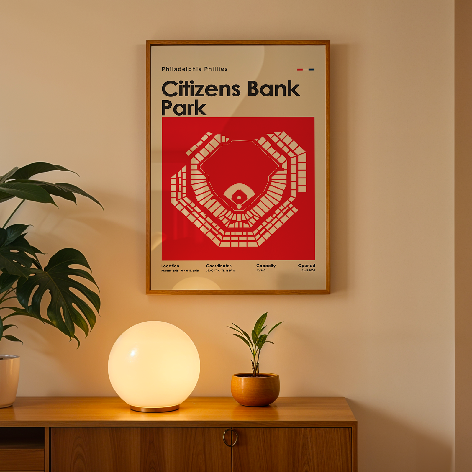 Framed poster of Citizens Bank Park on a wall above a wooden cabinet with decorative items.
