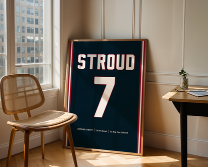 Framed sports jersey with 'STROUD' and number '7' in a room with a window and chair.