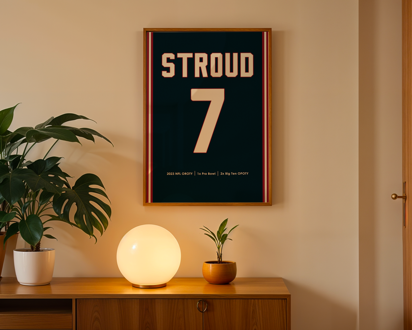 Framed poster with 'STROUD 7' on a wall above a wooden cabinet with decorative items.