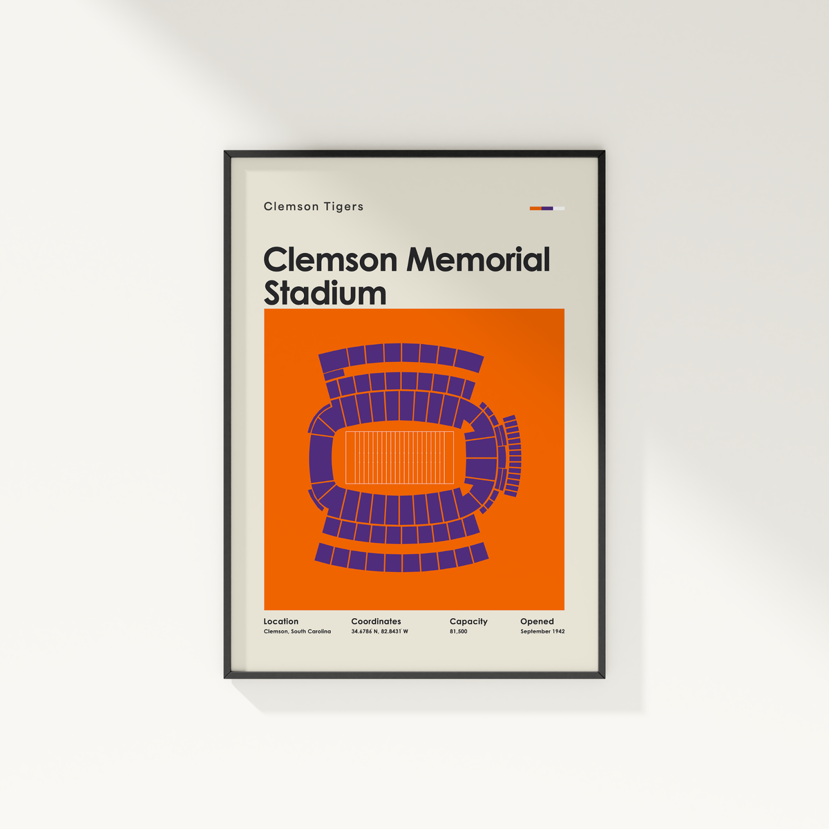 A framed Clemson Tigers Clemson Memorial Stadium poster on a light gray wall. The poster features a bold orange background with a purple stadium diagram and black text.