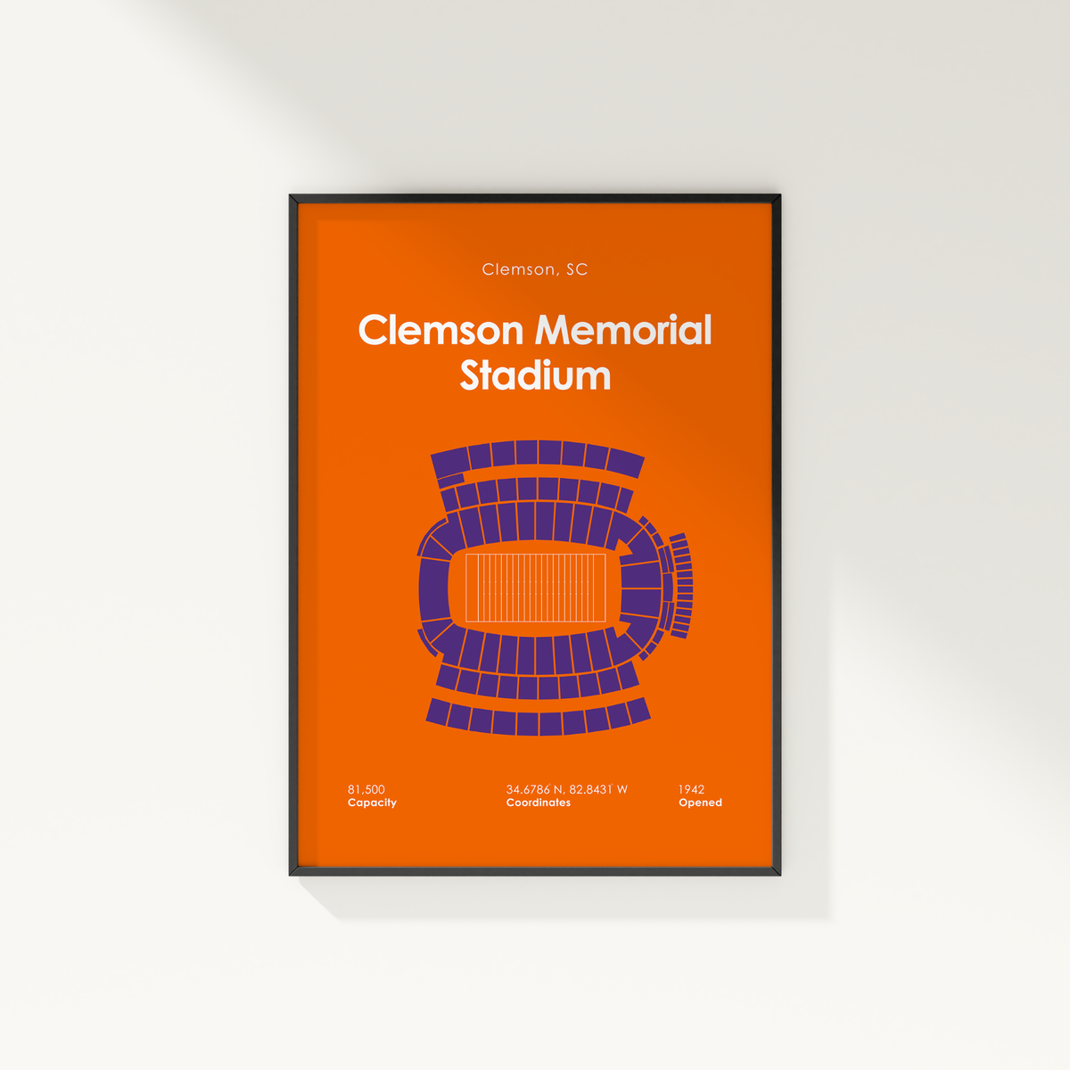 A framed Clemson University Memorial Stadium poster in orange and purple, shown hanging on a light gray wall with a soft shadow.