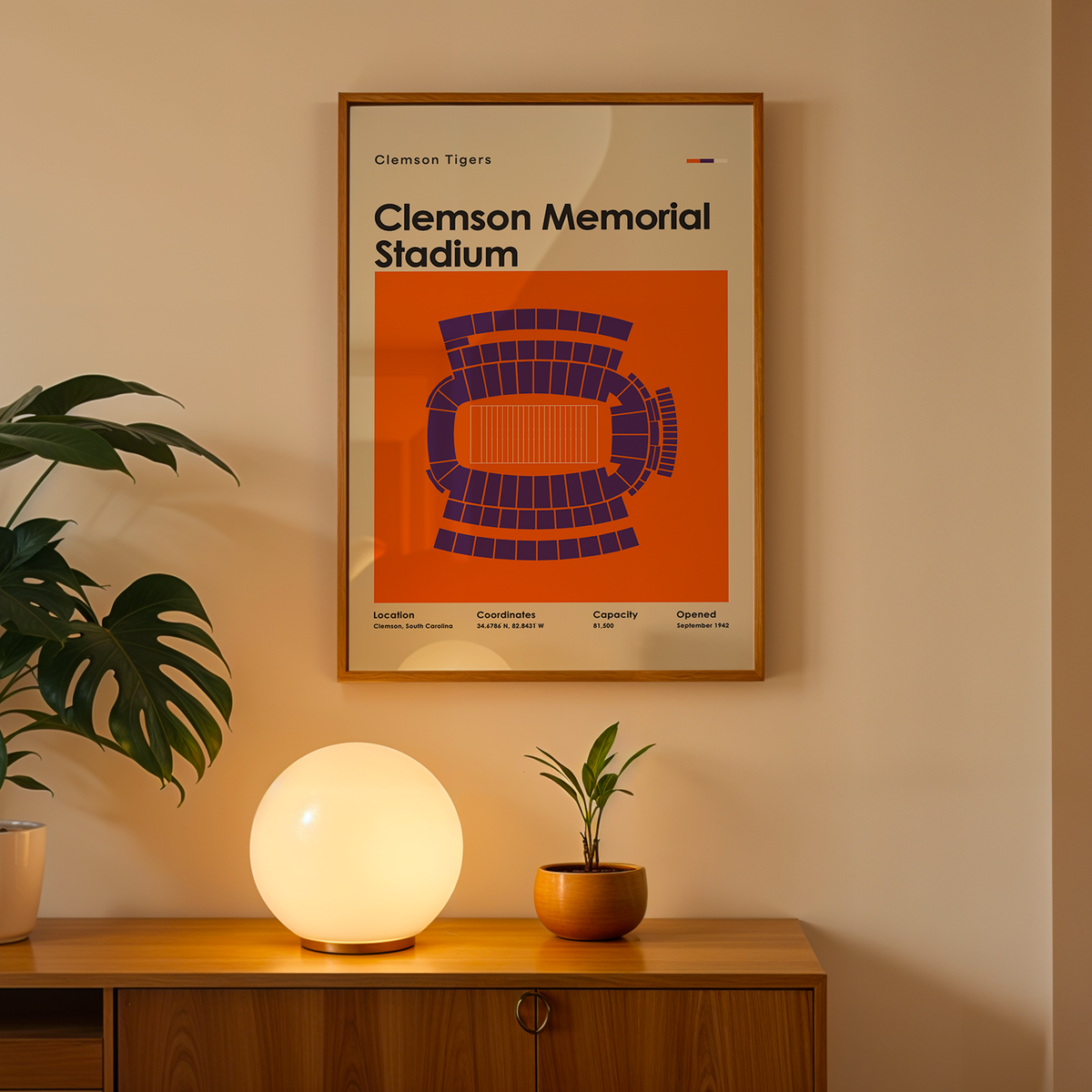 A framed Clemson Tigers 'Clemson Memorial Stadium' poster hangs on a beige wall above a wooden console table. The poster features an orange background with a blue stadium diagram.