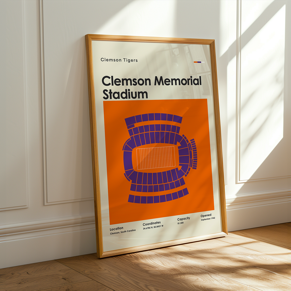 A framed Clemson Tigers 'Clemson Memorial Stadium' poster leaning against a white paneled wall on a light wood floor, with warm sunlight streaming in from a window.