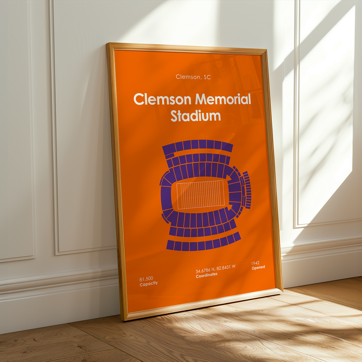 A framed Clemson University Clemson Memorial Stadium poster leans against a white paneled wall on a light wood floor, with warm sunlight casting shadows across the scene.