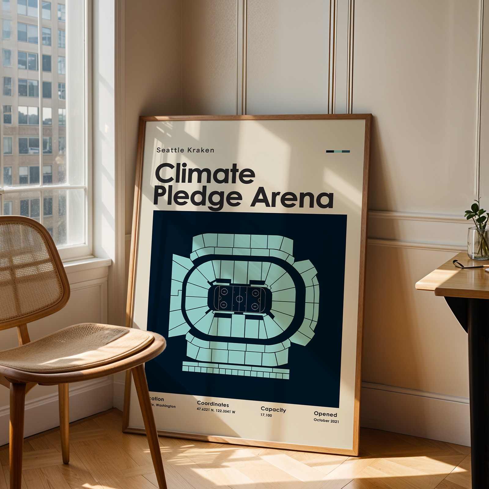 Framed poster of Climate Pledge Arena in a room with a chair and table.