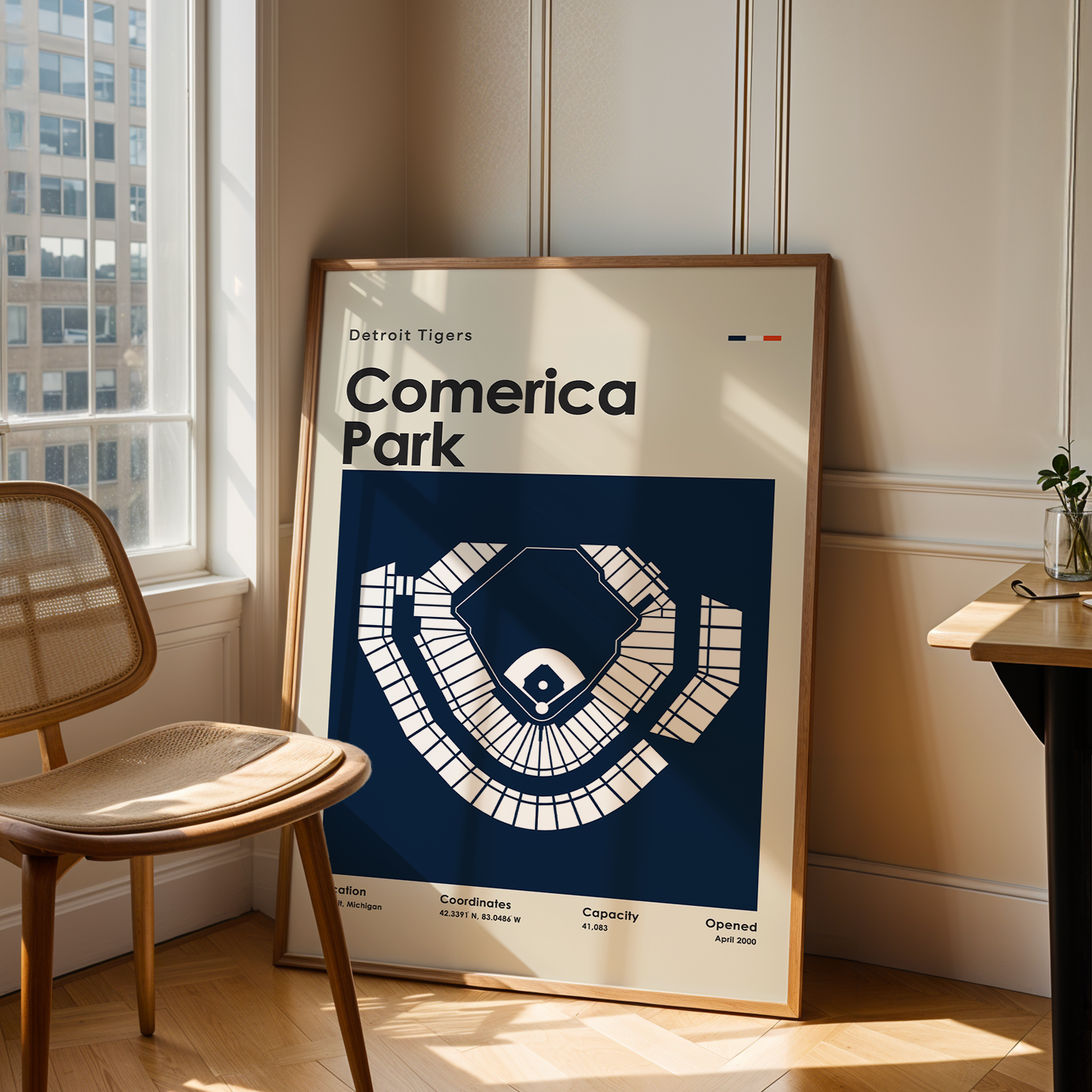 Framed poster of Comerica Park in a room with a chair and table.