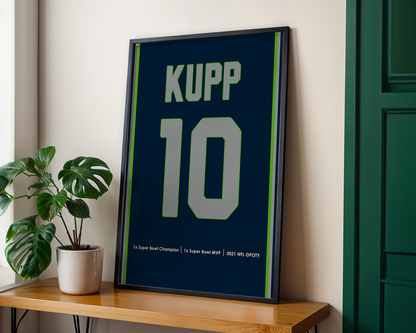 Framed sports jersey with 'KUPP 10' on a wooden shelf next to a plant.