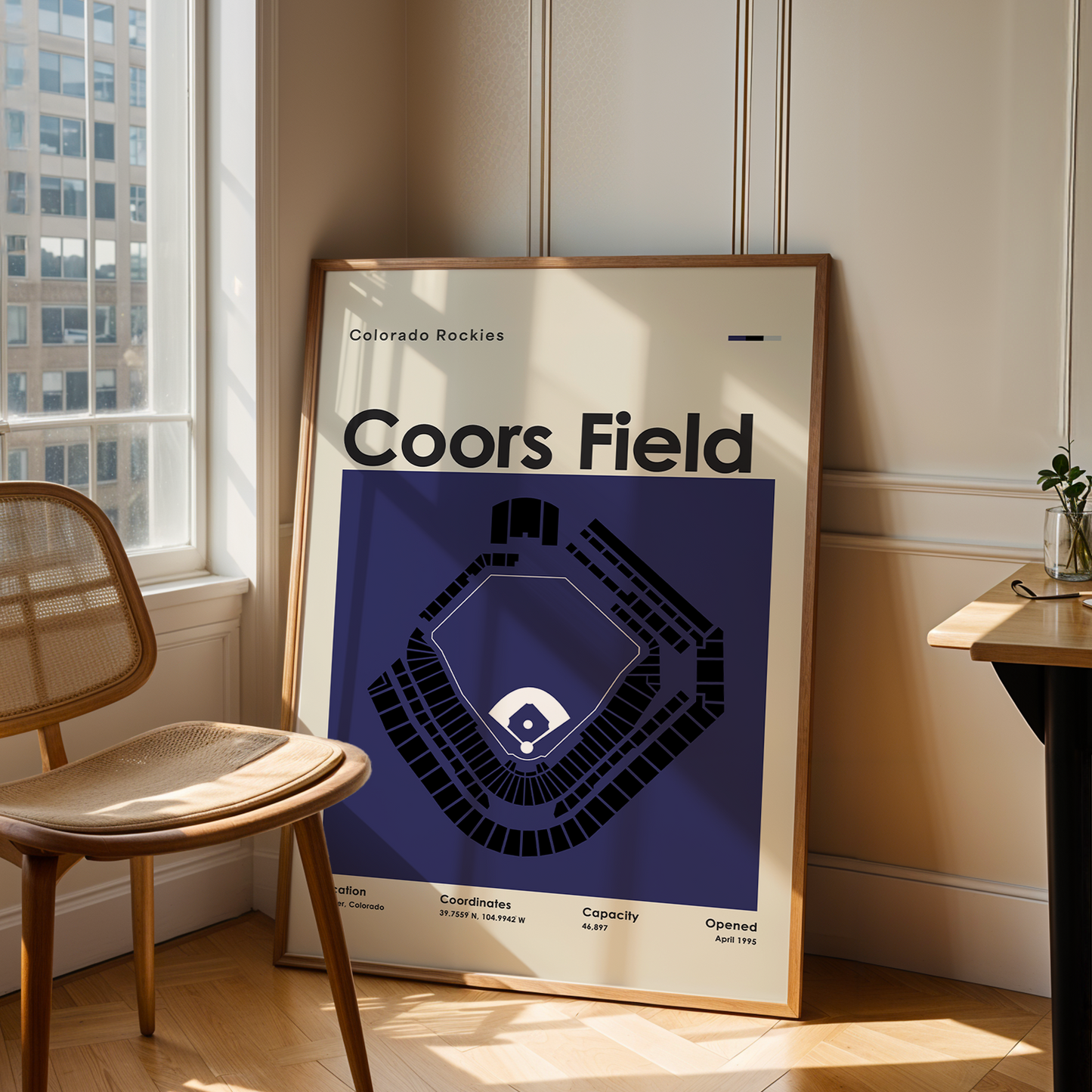 Framed Coors Field poster in a room with a chair and table.