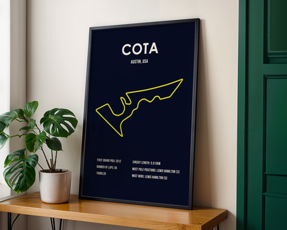 Framed poster with 'COTA' and race track outline on a wall next to a plant.