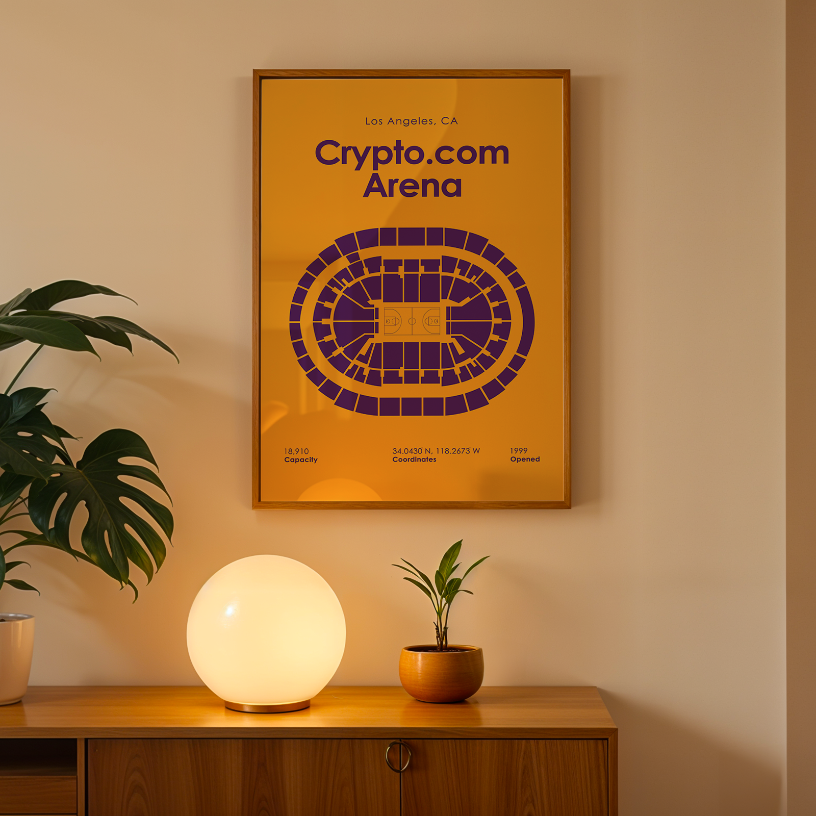 Framed 'Crypto.com Arena' poster on a wall with a plant and lamp on a wooden surface below.