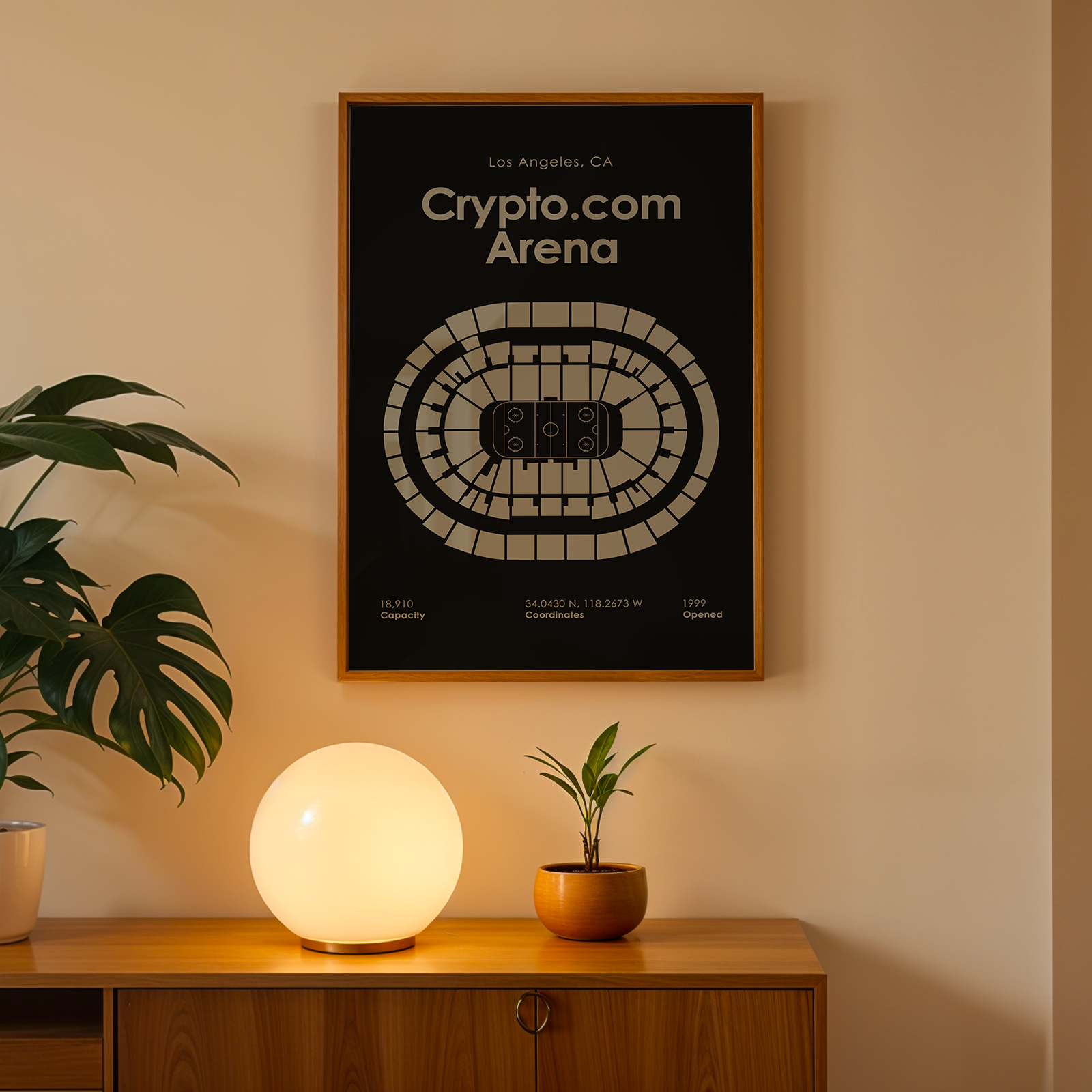Framed poster of Crypto.com Arena on a wall with a plant and lamp below.