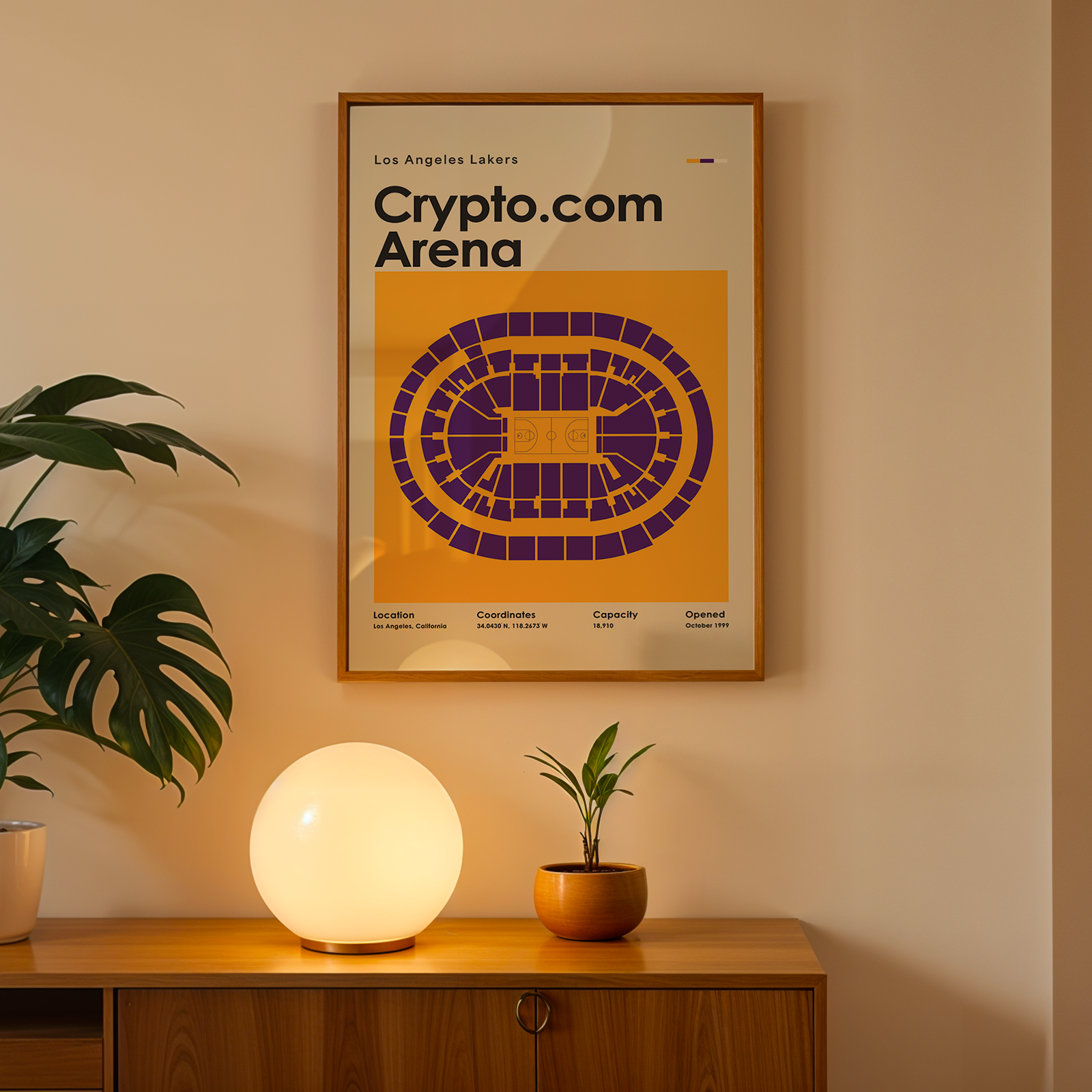 Framed poster of Crypto.com Arena on a wall above a wooden cabinet with decorative items.