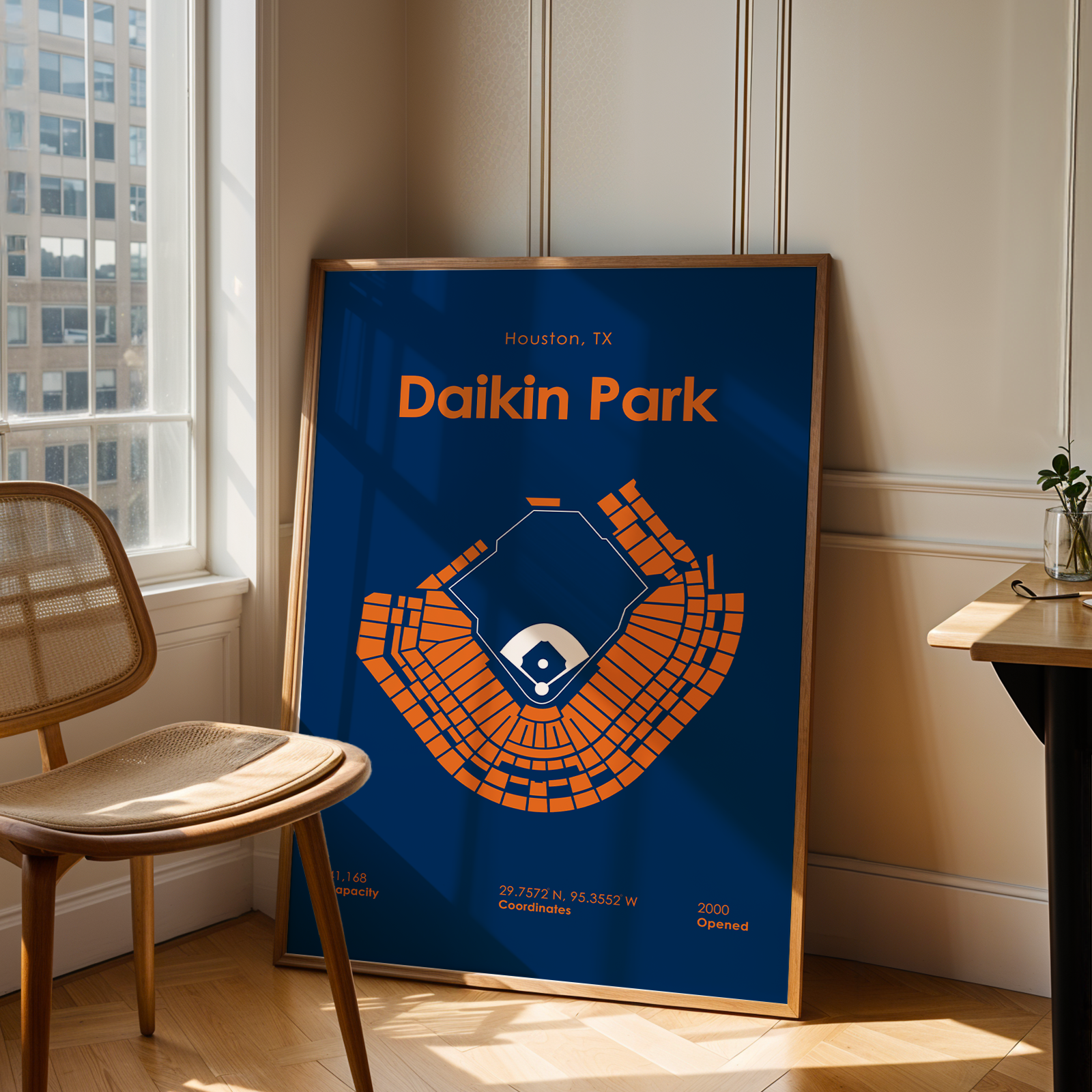 Framed poster of Daikin Park in Houston, TX, leaning against a wall in a room with a chair and window.