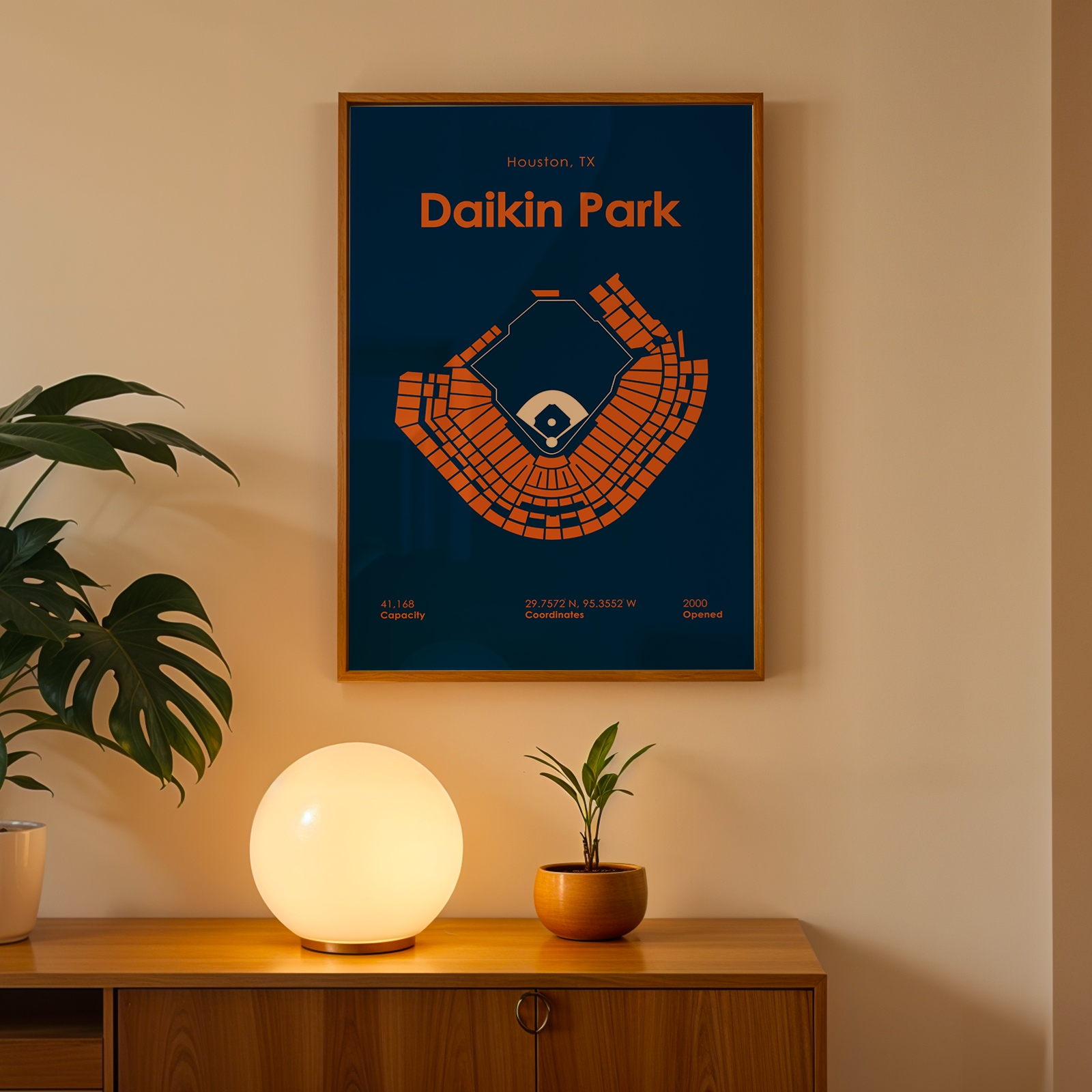 Framed poster of Daikin Park on a wall with a lamp and plant below.
