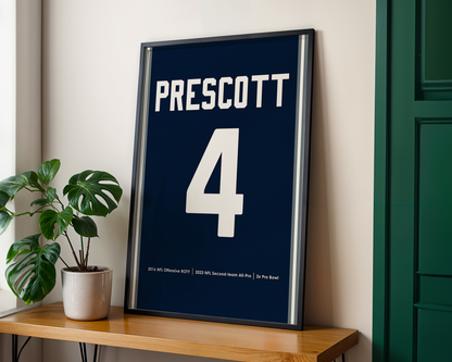 Framed sports poster with 'Prescott 4' on a wooden shelf.