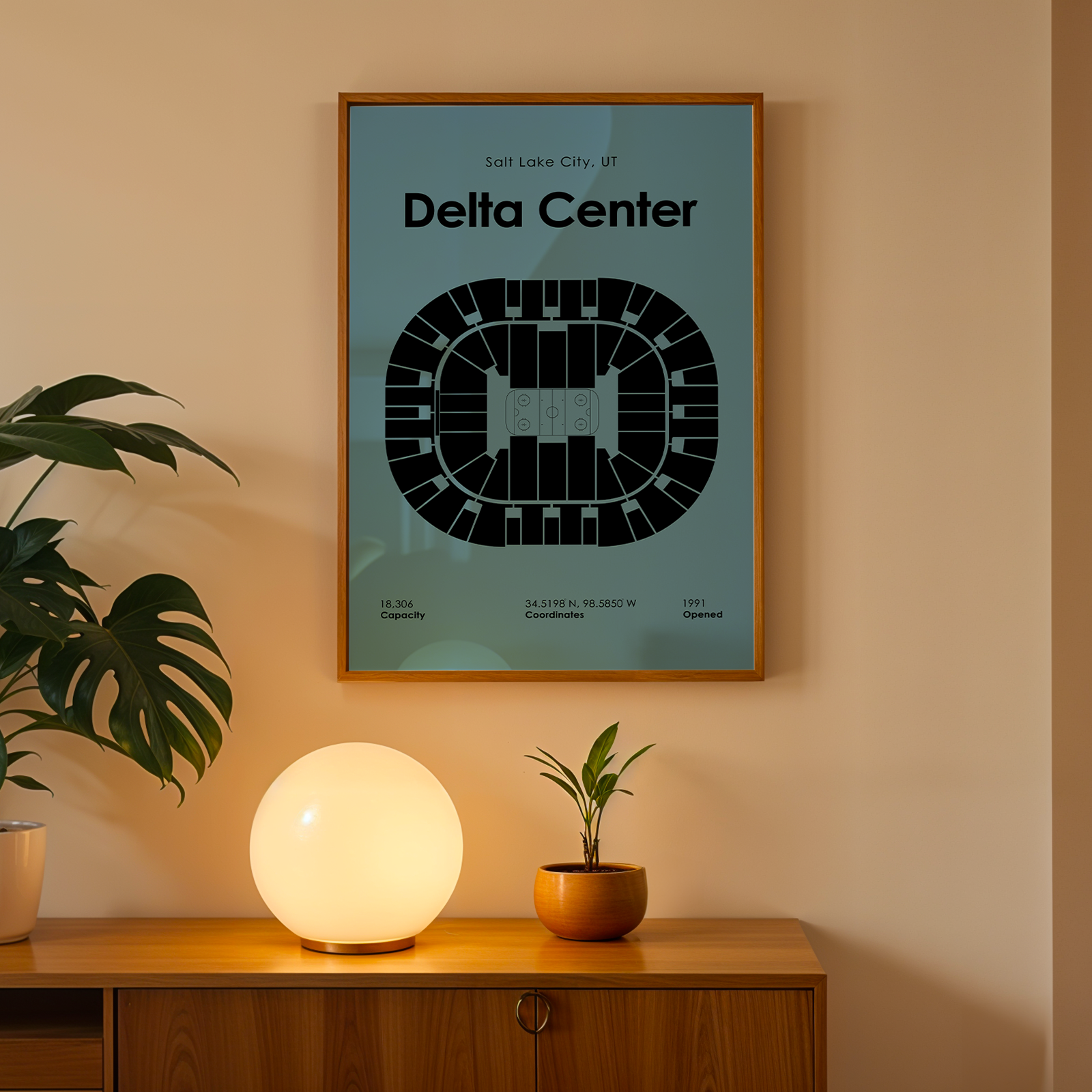 Framed poster of Delta Center on a wall with a plant and lamp below.
