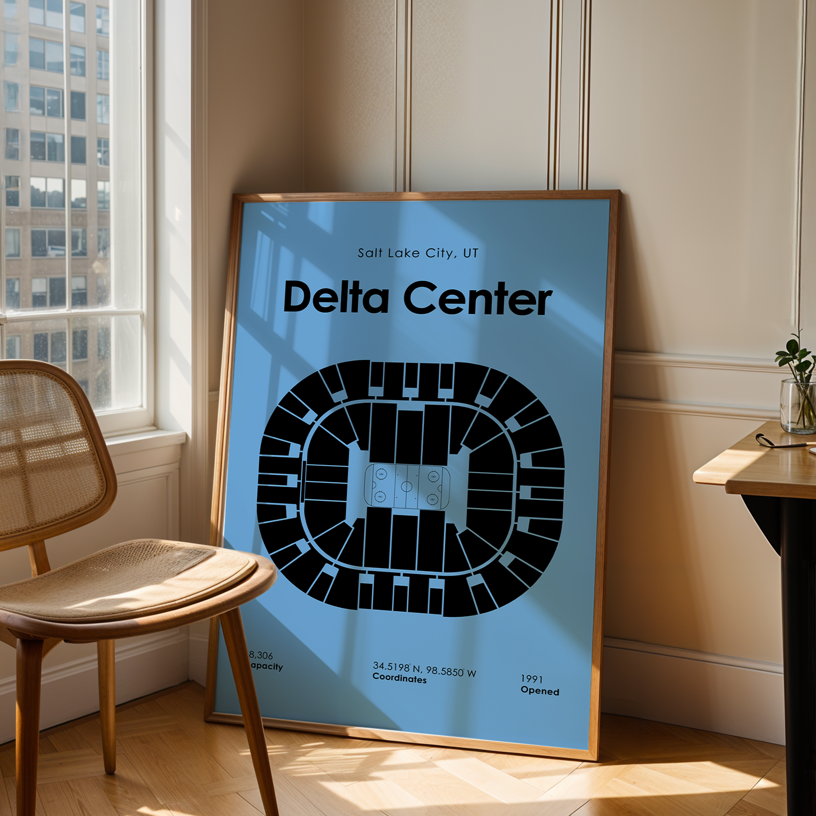 Framed poster of Delta Center in Salt Lake City, UT, leaning against a wall in a room with a chair and window.