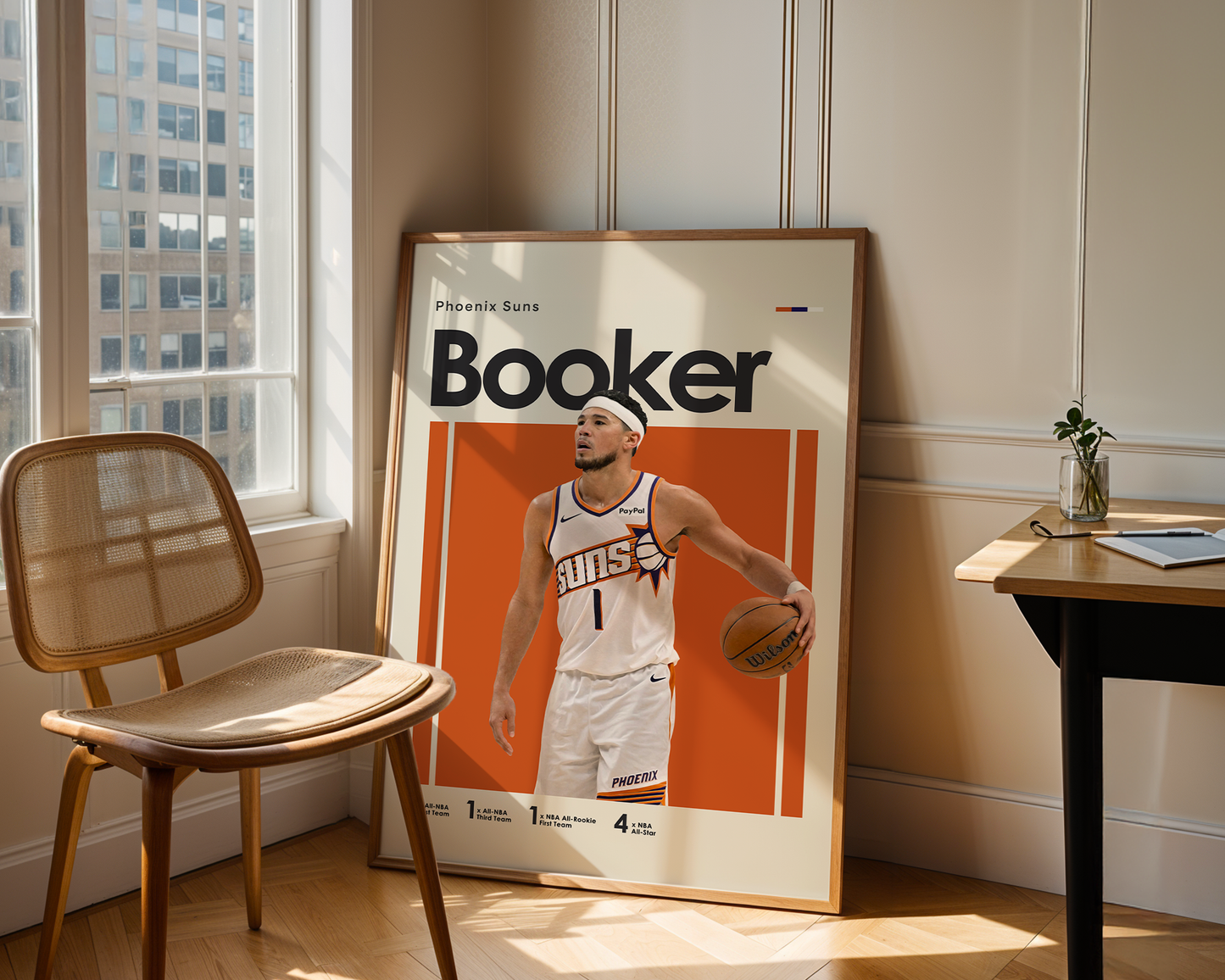 Framed poster of a basketball player named 'Booker' in a room with a chair and table.