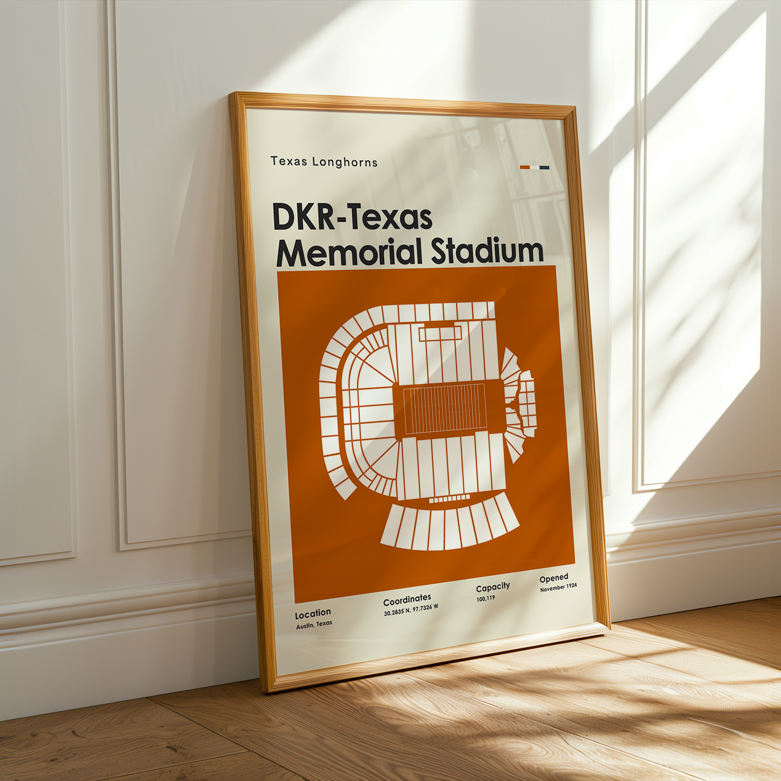 A framed art print of the Texas Longhorns at DKR-Texas Memorial Stadium leans against a white paneled wall on a light wood floor, with warm sunlight casting shadows across the wall and floor.