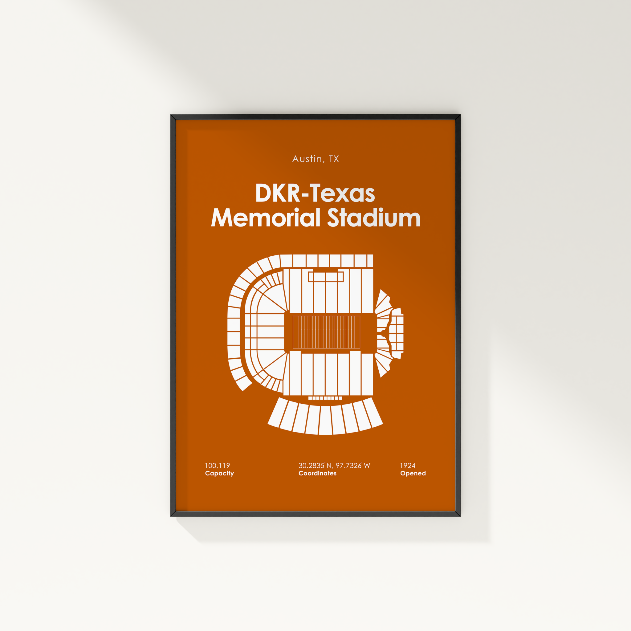 A framed minimalist stadium floor plan poster for DKR-Texas Memorial Stadium in Austin, TX, featuring a white schematic on a burnt orange background, shown hanging on a light wall.