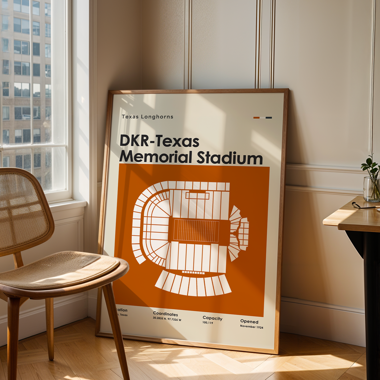 A framed vintage-style sports poster for DKR-Texas Memorial Stadium leans against a wall in a sunlit room with a wooden chair and desk.