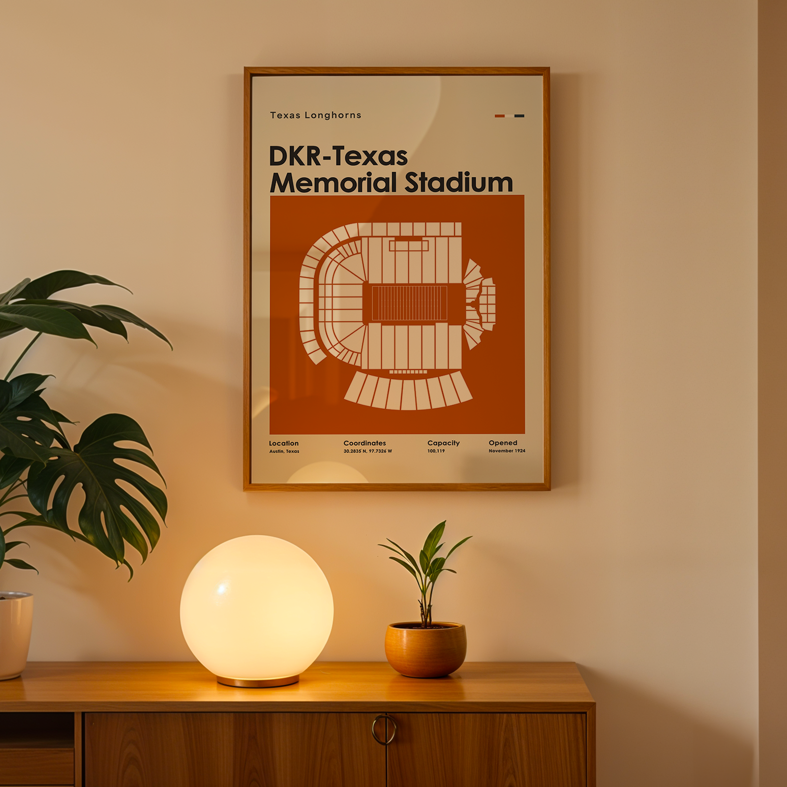 A framed poster of the DKR-Texas Longhorns Memorial Stadium seating plan hanging on a beige wall above a wooden console table with a glowing globe lamp and potted plants.