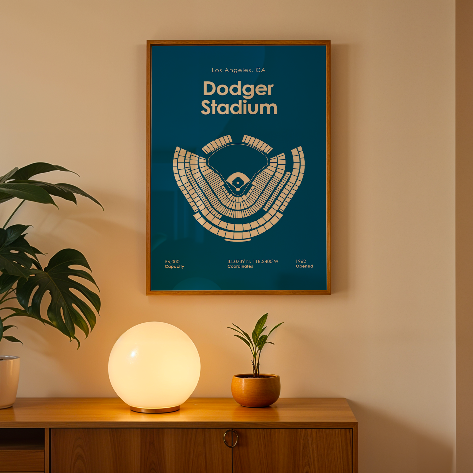 Framed poster of Dodger Stadium on a wall with a plant and lamp below.
