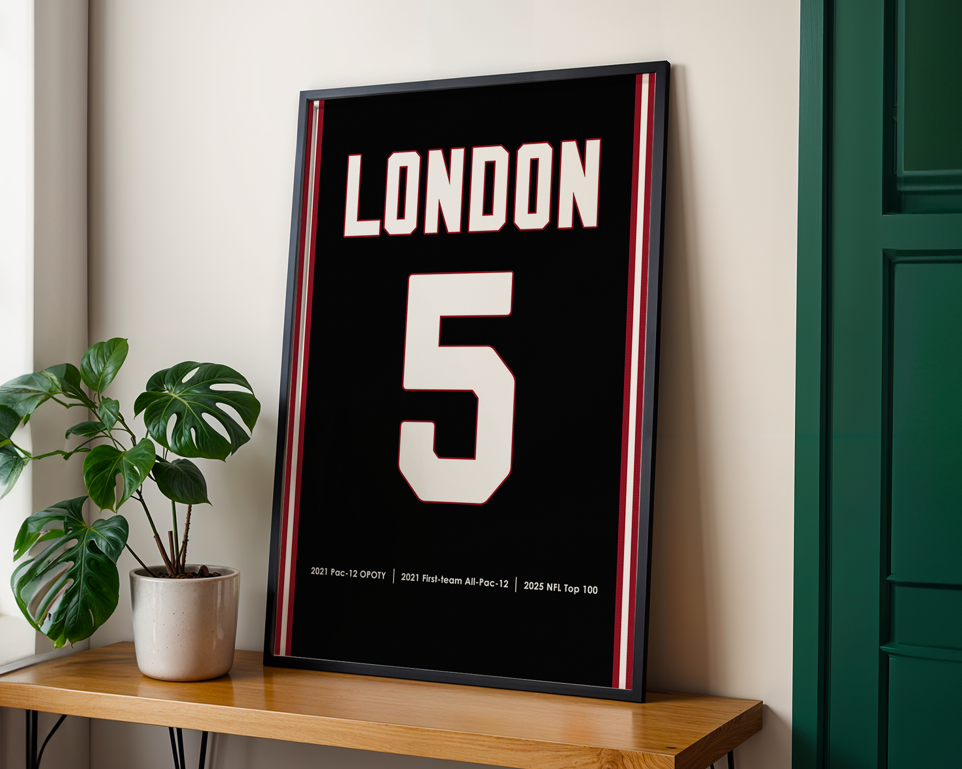 Framed poster with 'London' and number '5' on a wall next to a plant and wooden shelf.