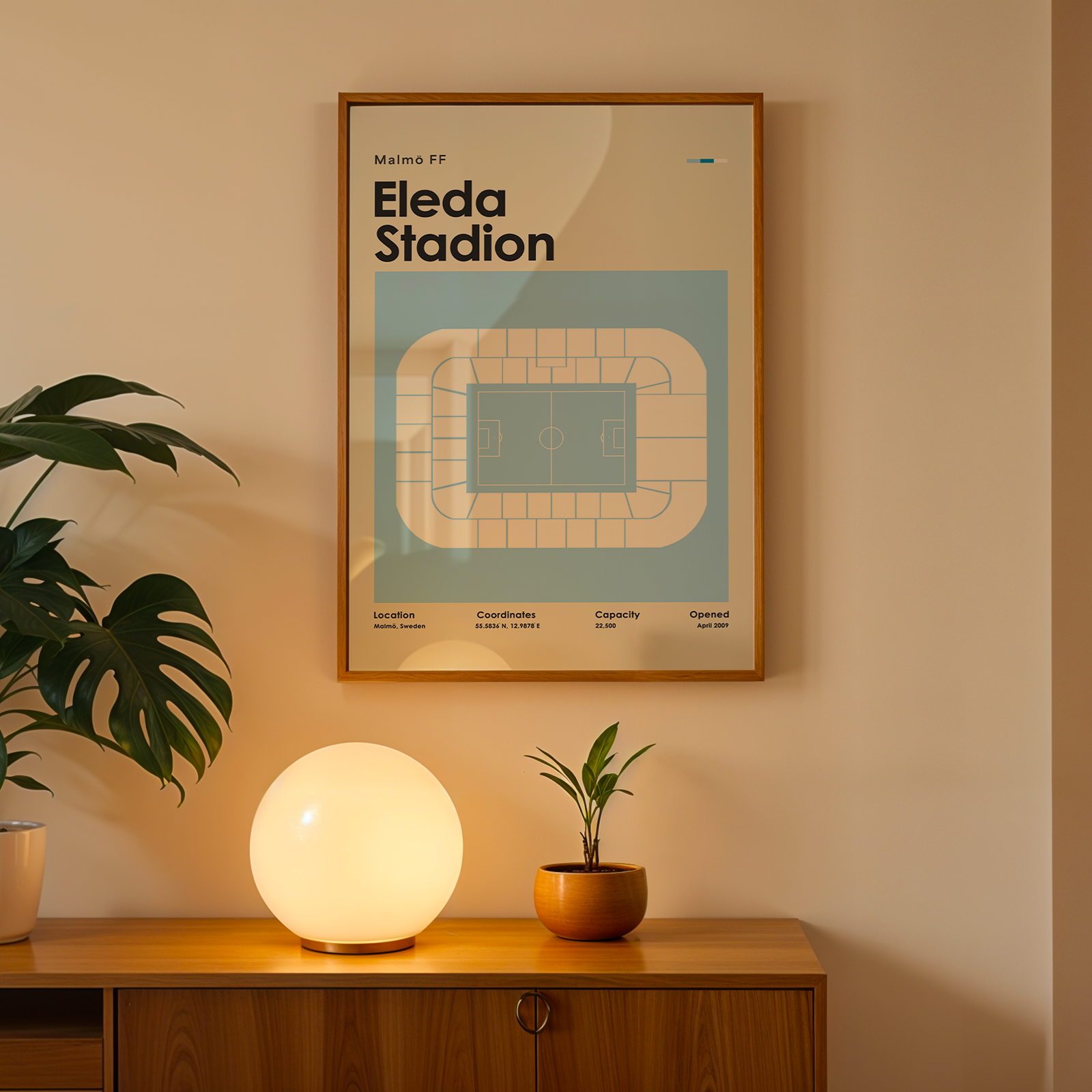 Framed poster of Eleda Stadium on a wall above a wooden cabinet with decorative items.