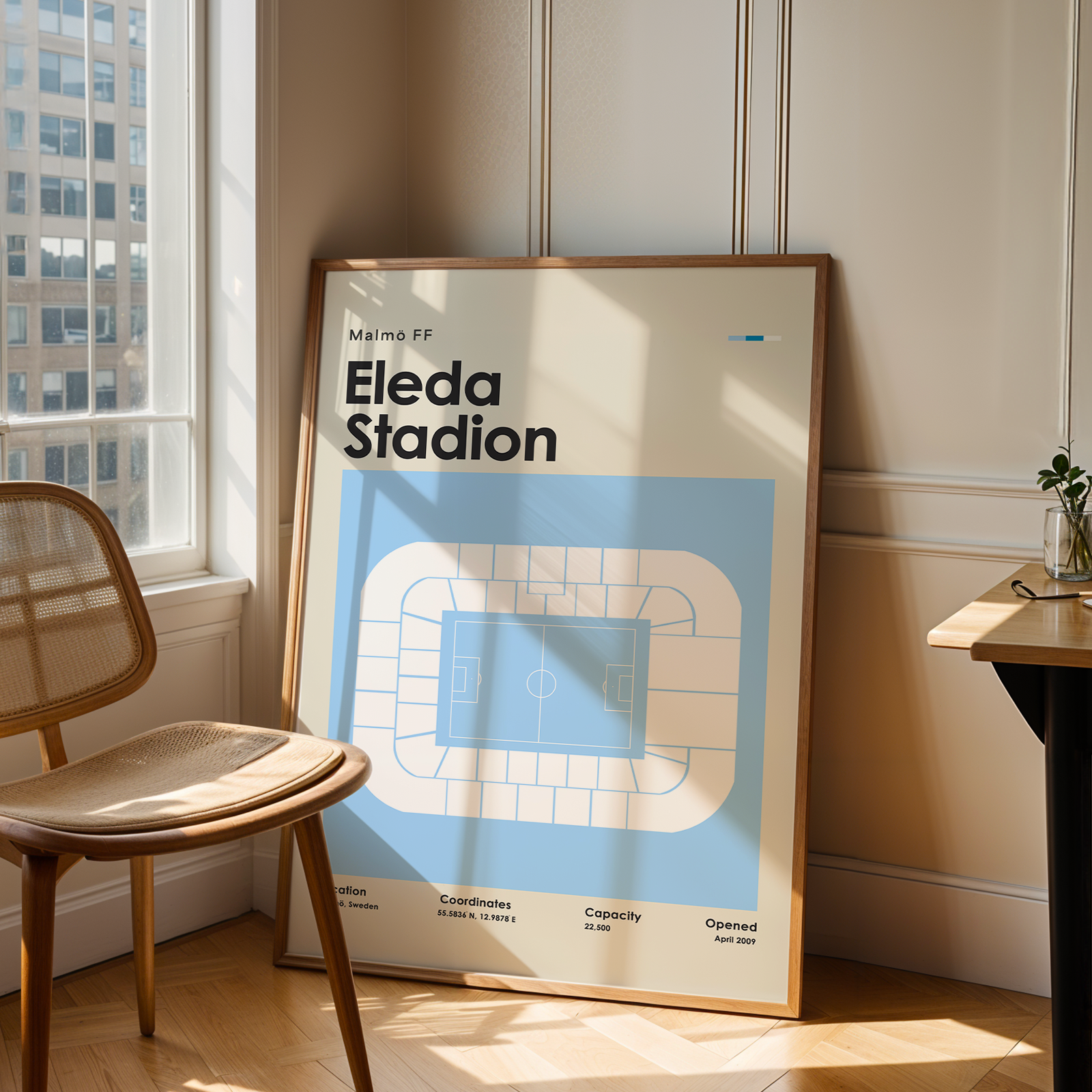 Framed poster of Eleda Stadion in a room with a chair and window.