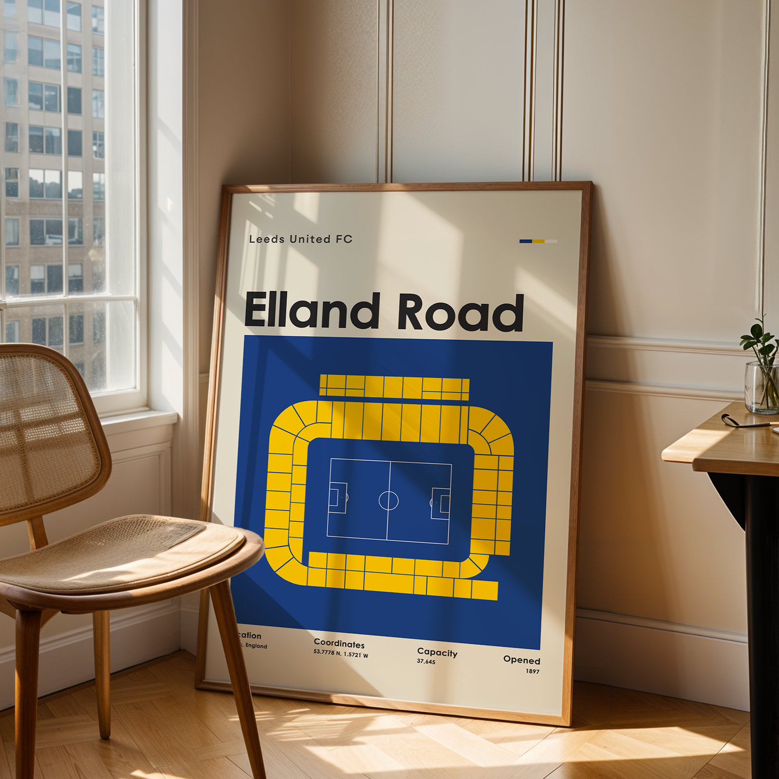 Framed poster of Elland Road stadium in a room with a chair and table.
