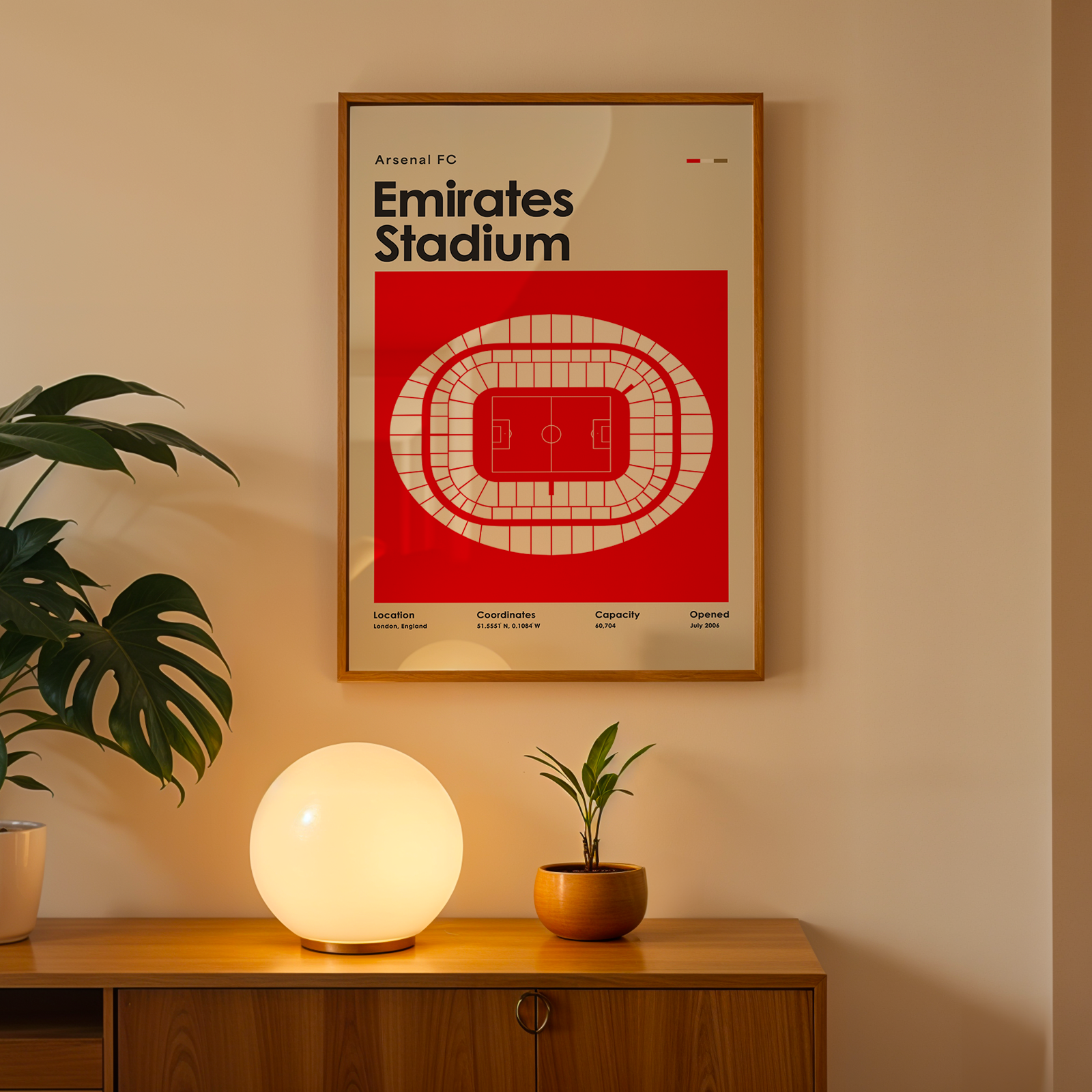 Framed Arsenal FC Emirates Stadium poster on a wall with a wooden cabinet and decorative items below.