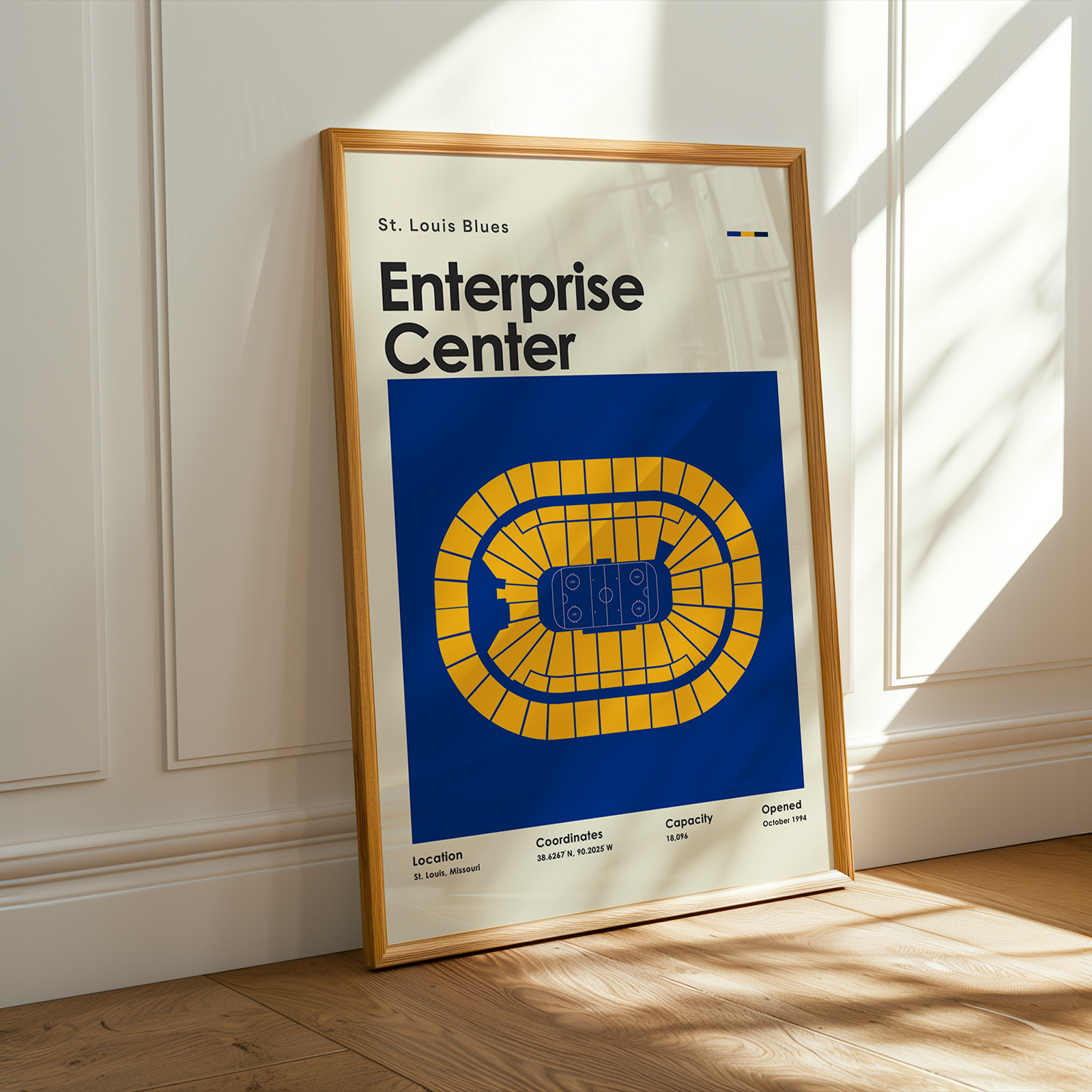 Framed poster of St. Louis Blues Enterprise Center on a wooden floor with sunlight streaming through a window.