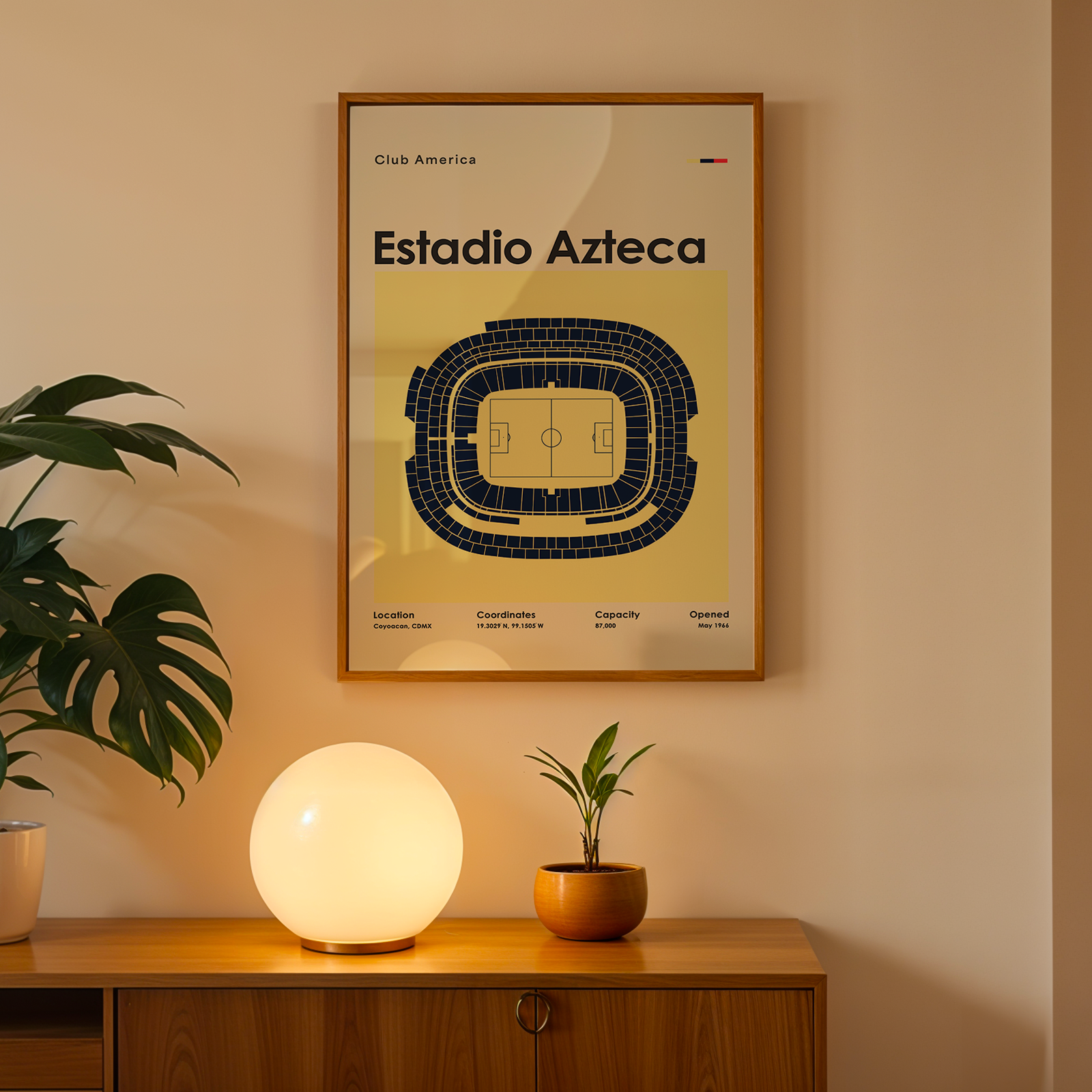A framed Club America Estadio Azteca sports poster hanging on a beige wall above a wooden console table. The poster features a dark blue stadium layout on a pale yellow background.