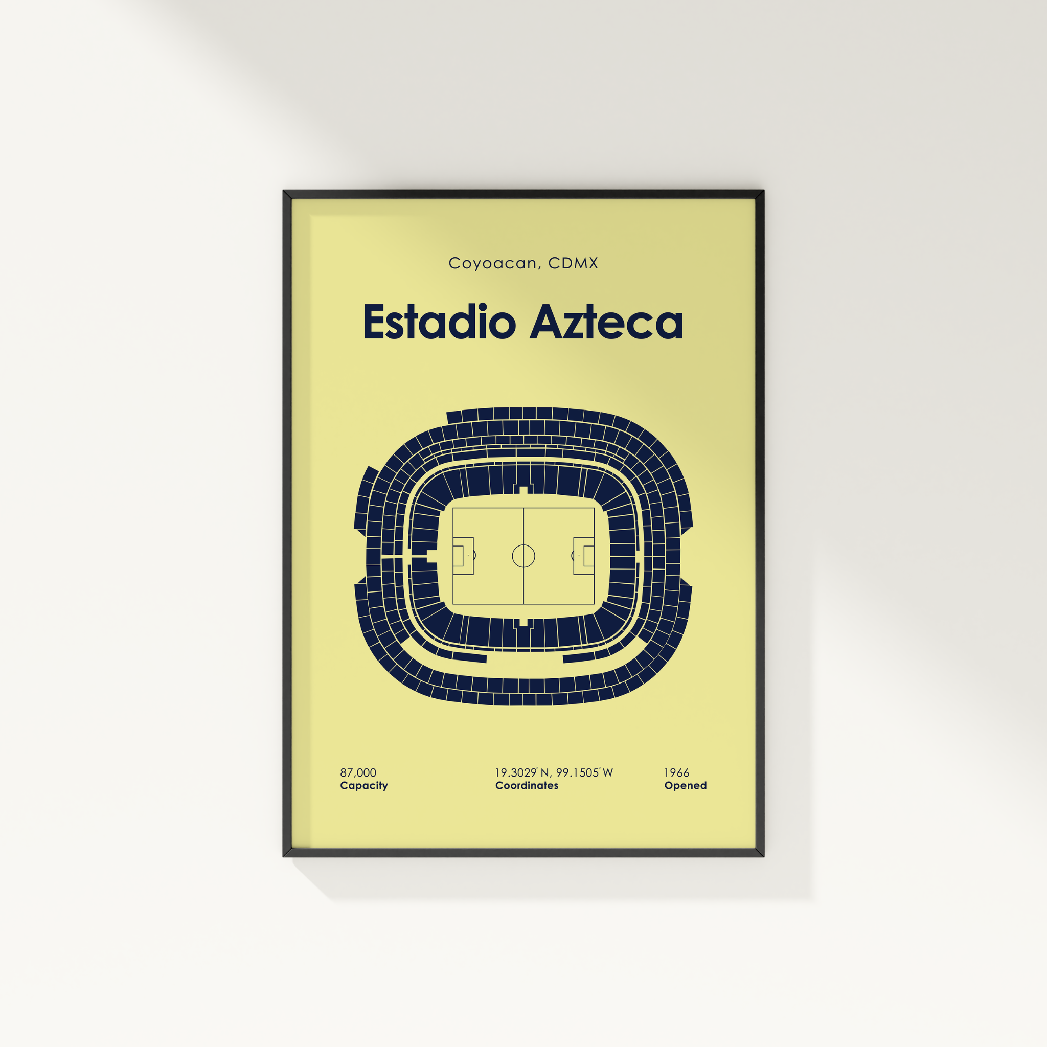 A framed sports poster of Estadio Azteca, featuring a dark blue stadium floor plan on a pale yellow background, shown hanging on a white wall.