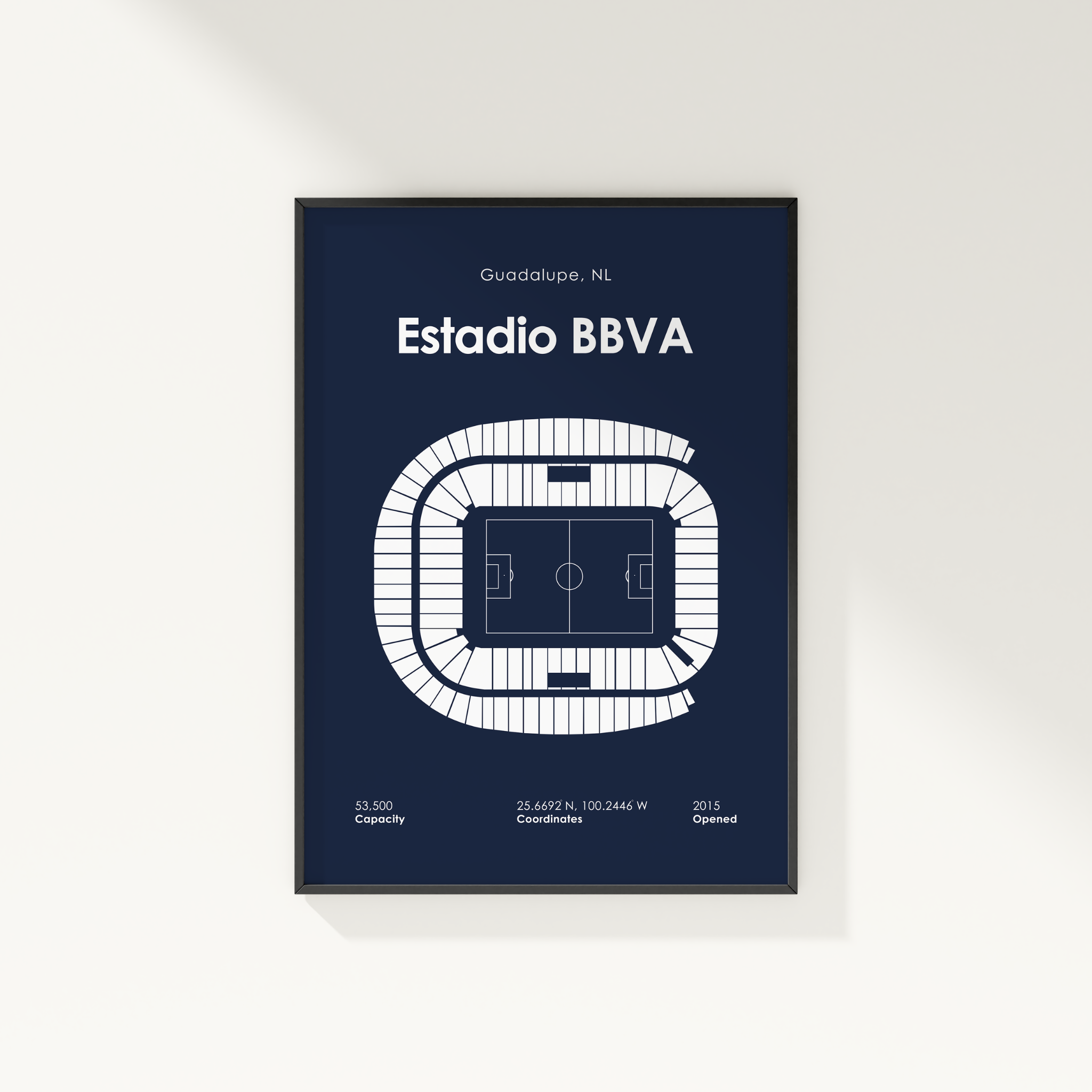 A framed minimalist stadium floor plan poster of Estadio BBVA in Guadalupe, NL, featuring a white vector diagram of the stadium on a dark navy blue background, shown hanging on a light beige wall.