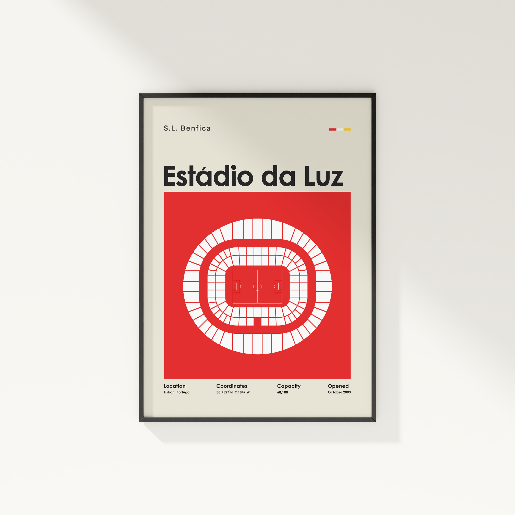 A framed minimalist poster of Estãdio da Luz in Lisbon, Portugal, featuring a red and white stadium diagram on a light beige background, shown hanging on a white wall.