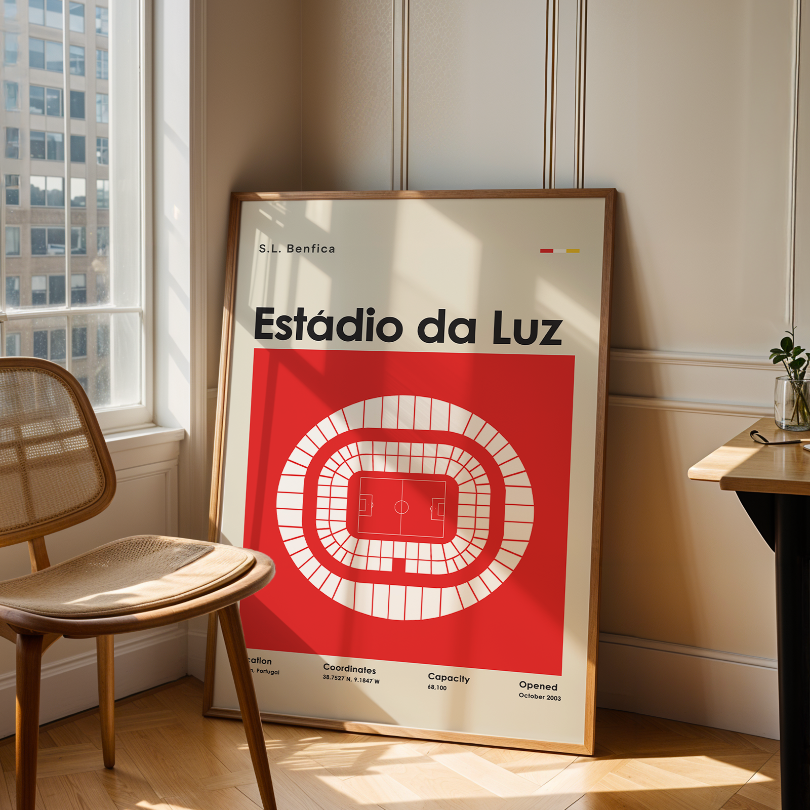 A framed poster leaning against a wall in a sunlit room, featuring a red and white stadium diagram with the text 'Estãdio da Luz'