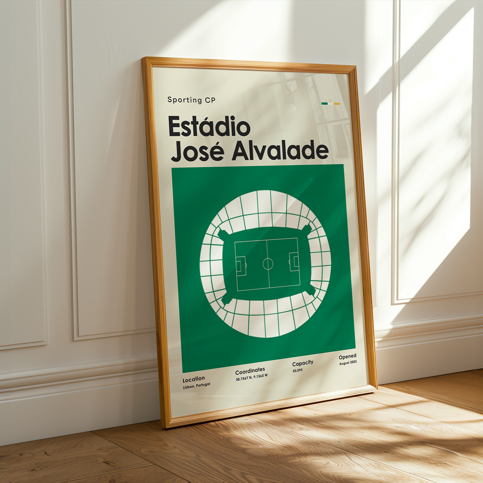 A framed sports poster of Estádio José Alvalade, featuring a green and white stadium diagram, leaning against a white paneled wall on a wooden floor with warm sunlight streaming in.