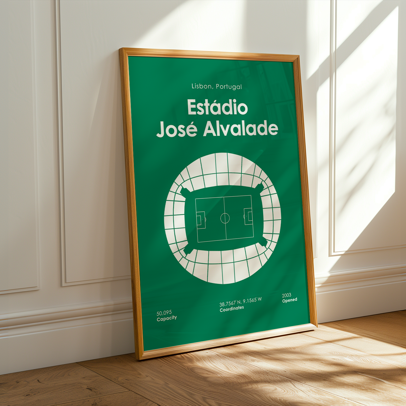 A framed sports poster of Estãdio Jóse Alvalade in Lisbon, Portugal, leaning against a white paneled wall on a wooden floor with warm sunlight streaming in.