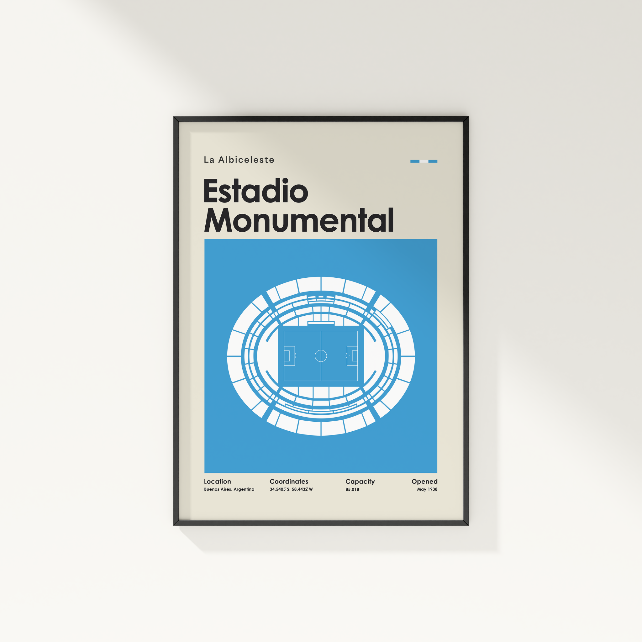 A framed minimalist poster of the Estadio Monumental in La Albiceleste, featuring a blue and white stadium diagram on a light beige background, shown hanging on a white wall.