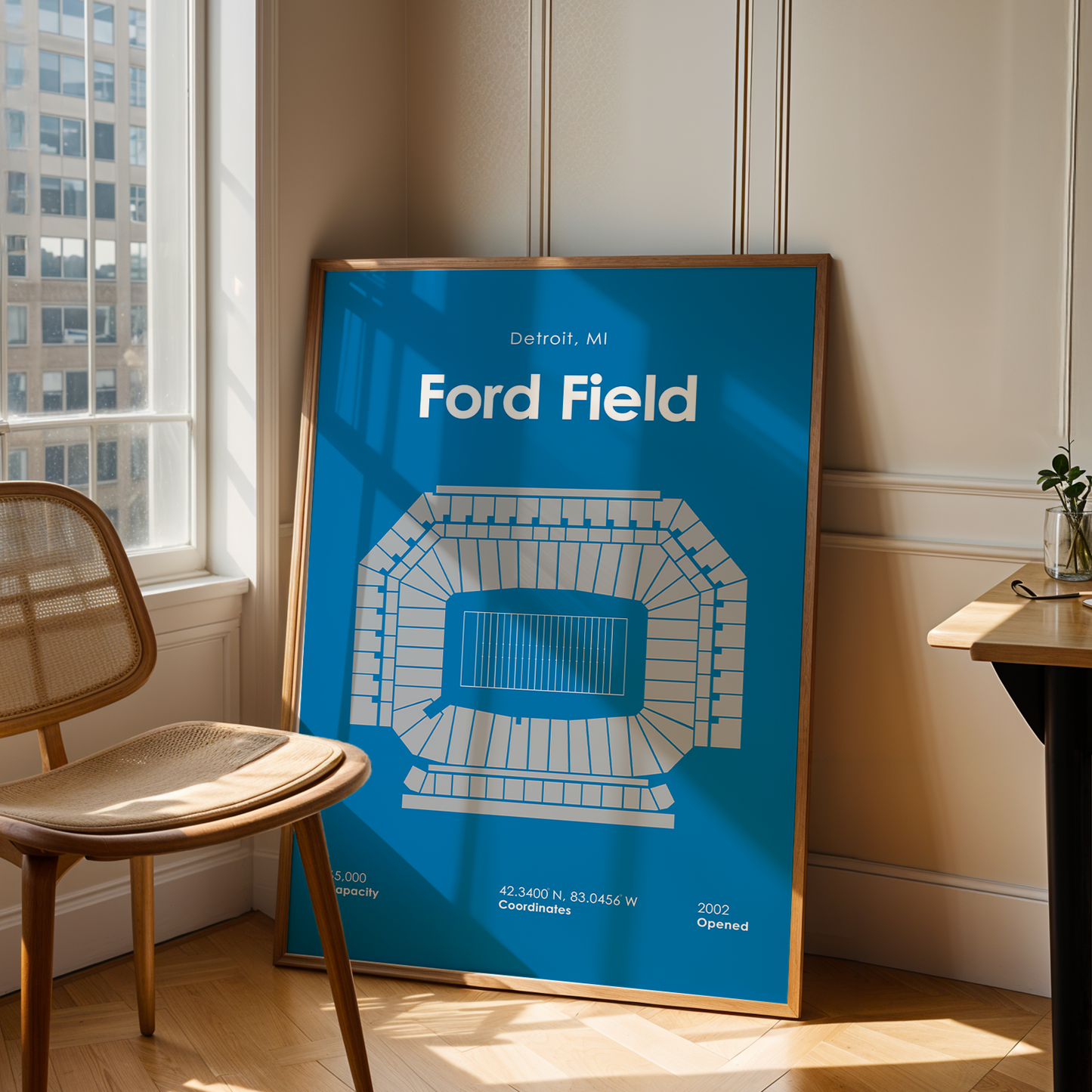 Framed poster of Ford Field in a room with a chair and table.