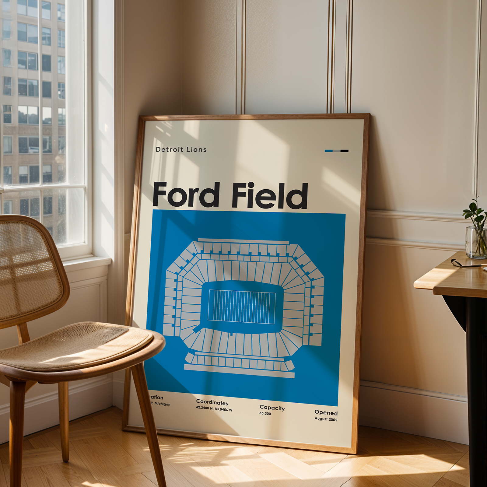 Framed poster of Ford Field in a room with a chair and window.