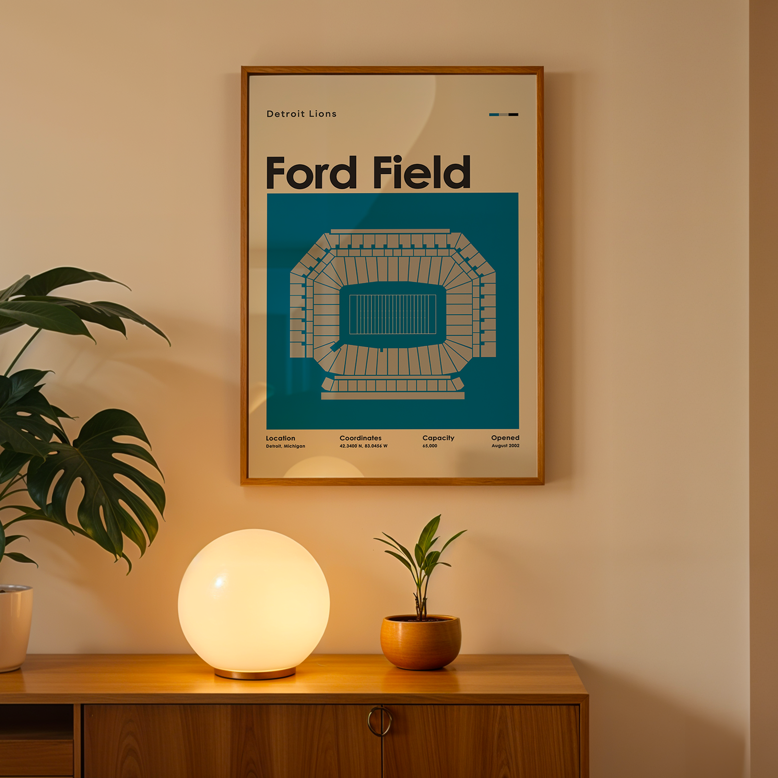 Framed poster of Ford Field on a wall above a wooden cabinet with decorative items.