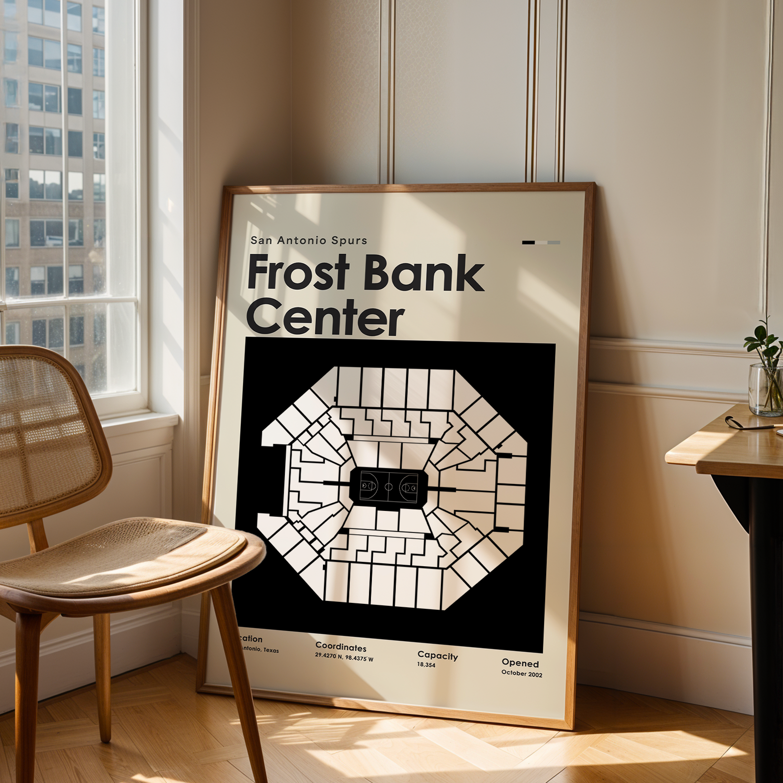 Framed poster of Frost Bank Center in a room with a chair and table.