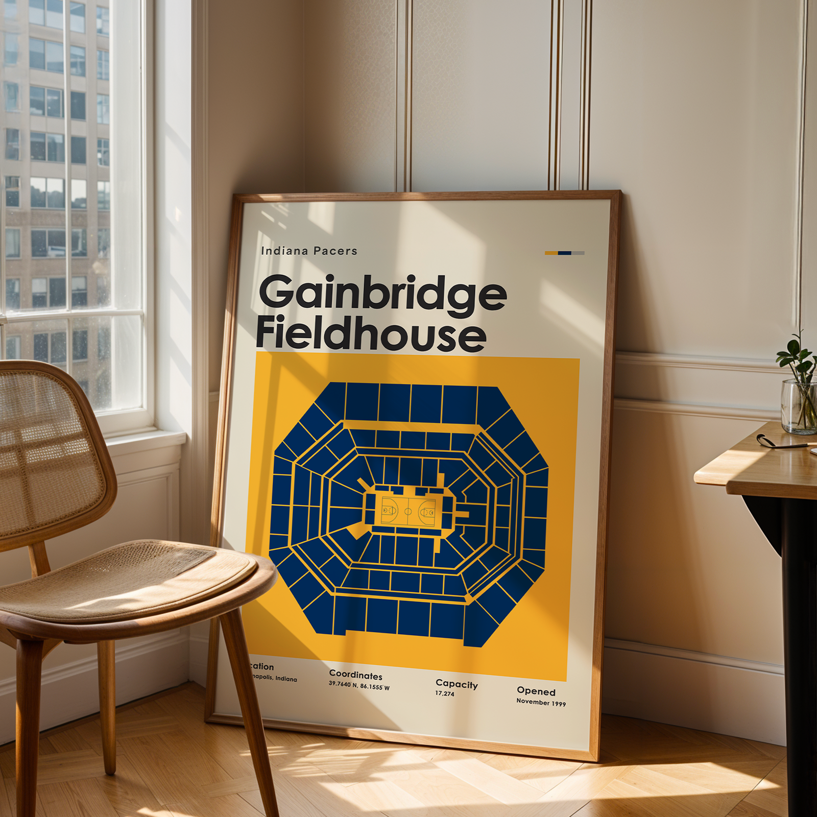 Framed poster of Gainbridge Fieldhouse in a room with a chair and table.