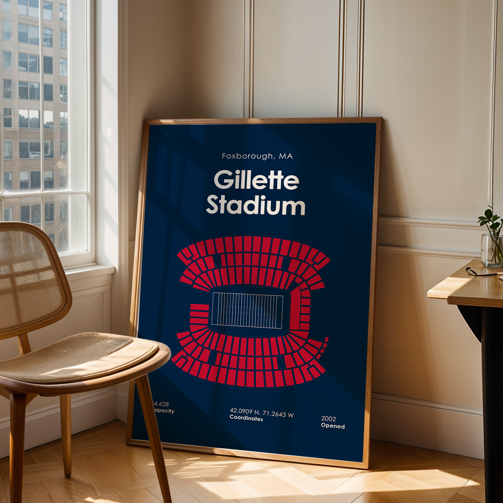 Framed poster of Gillette Stadium in a room with a chair and table.
