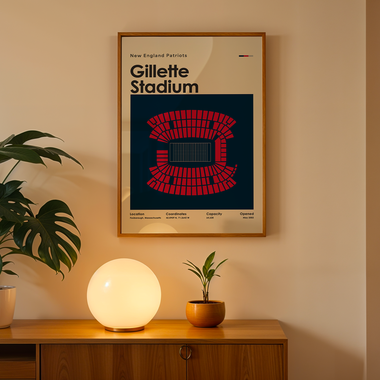 Framed poster of Gillette Stadium on a wall above a wooden cabinet with decorative items.