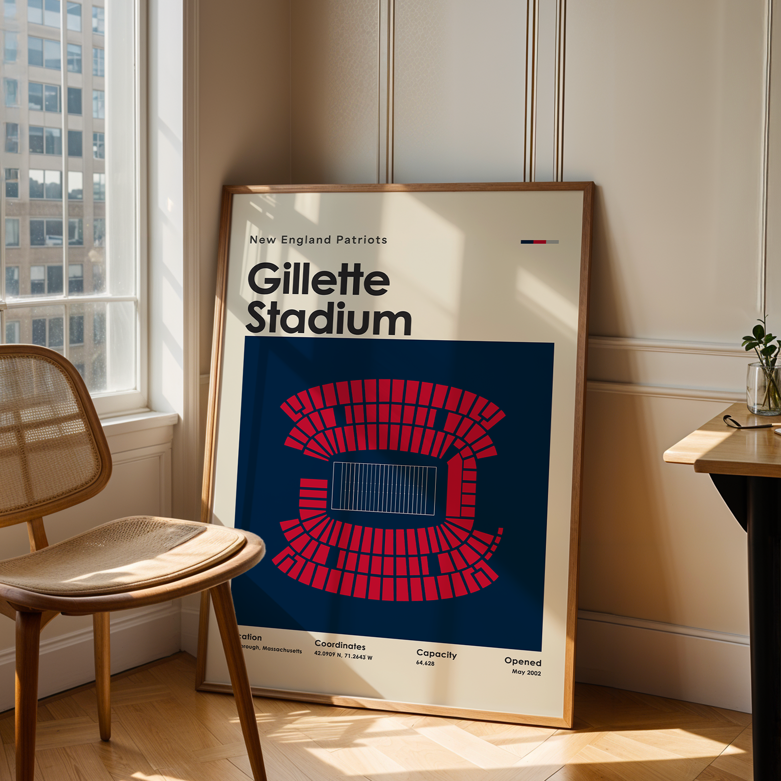 Framed poster of Gillette Stadium in a room with a window and chair.