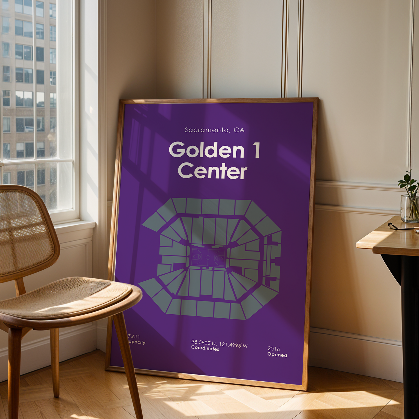 Framed poster of Golden 1 Center in Sacramento, CA, leaning against a wall in a room with a chair and table.